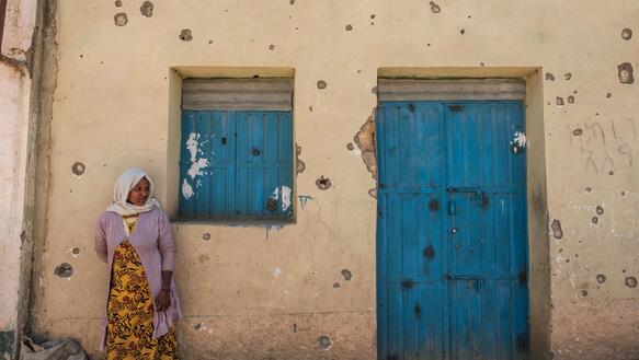 Eine Frau steht vor einer Hauswand mit vielen Einschusslöchern
