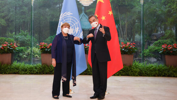 Das Bild zeigt zwei Personen vor der UN-Flagge und der chinesischen Flagge, sie schauen in die Kamera