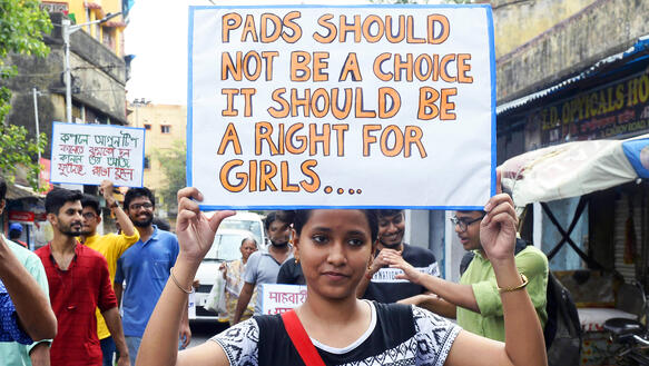 Das Bild zeigt eine junge Frau bei einer Demonstration, die ein Schild nach oben hält