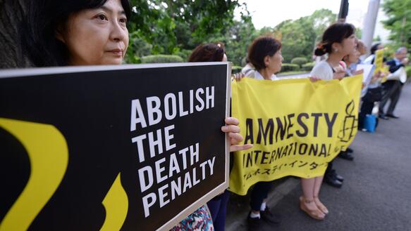 Das Bild zeigt mehrere Menschen, die mit Schildern demonstrieren, darauf steht "Schafft die Todesstrafe ab"