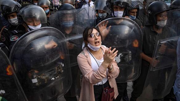 Eine Frau steht zwischen zahlreichen uniformierten Polizisten mit Schildern und klatscht.