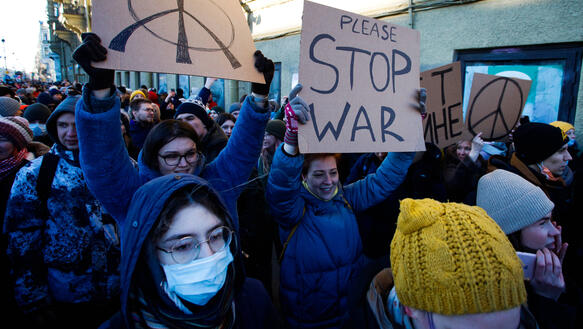 Das Bild zeigt mehrere Menschen mit Plakaten in der Hand, darauf zu lesen "Stop War"
