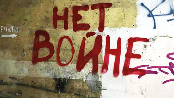 An einer Wand ist ein Grafitto aufgesprüht, geschrieben steht dort "HETBONHE", übersetzt: "Kein Krieg".
