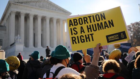 Das Bild zeigt eine Menge an Demonstrierenden vor einem Gebäude. Eine Person hält ein Amnesty-Schild mit der Aufschrift: "Abortion is a human right".