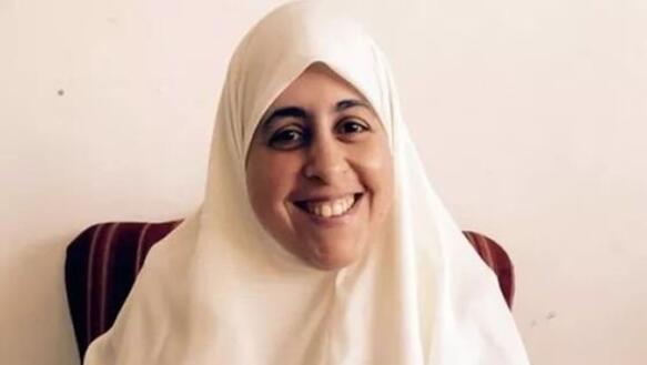 Porträtfoto von Aisha el-Shate, die auf einem Stuhl sitzt und ein Kopftuch trägt und in die Kamera lächelt.