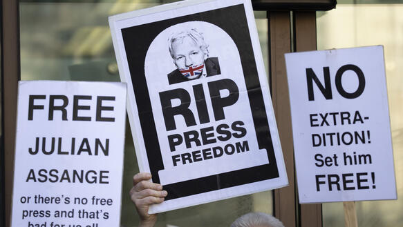Personen halten bei einer Demonstration Schilder hoch, auf denen unter anderem steht: "Free Julian Assange" oder "RIP press freedom".