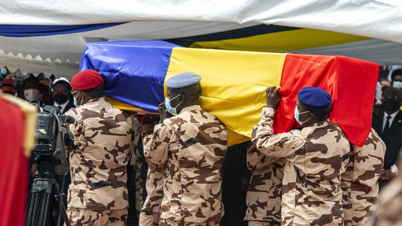 Sechs uniformierte Soldaten tragen einen Sarg, der mit der tschadischen Flagge umwickelt ist.