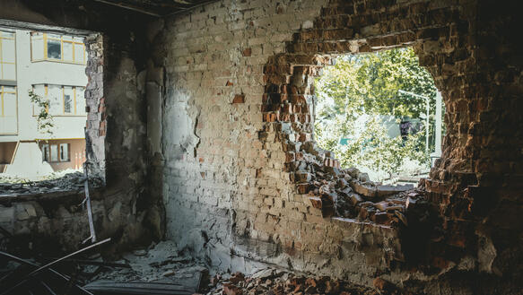 Eine zerstörte Wohnung, die Backsteine sind offengelegt, eine Wand kreisförmig durchschlagen worden von einem Geschoss.