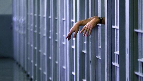 Eine Person hält ihre Hände aus den Gitterstäben ihrer Gefängniszelle.