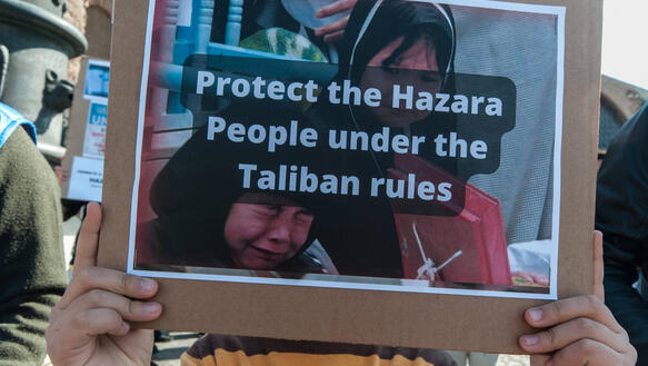 Das Bild zeigt eine Person, die ein Plakat in der Hand hält, auf dem steht: "Protect the Hazara People under the Taliban rules"