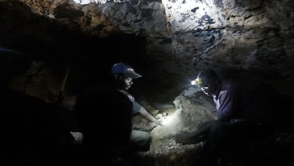 Das Bild zeigt zwei Personen mit Stirnlampen in einer dunklen Höhle. Sie arbeiten.