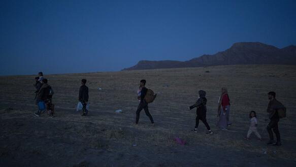 Männer, Frauen und Kinder laufen über eine Steppe in einer Hügellandschaft bei Nacht.