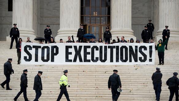 Das Bild zeigt mehrere Menschen, die ein großes Banner mit der Aufschrift "Stop Executions" in der Hand halten