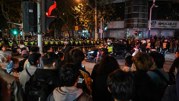 Das Bild zeigt eine Menschenmenge, die vor Polizisten steht
