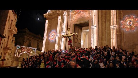 Das Bild zeigt eine Szene vor einer Kirche, viele Menschen stehe davor, sie tragen ein Kreuz