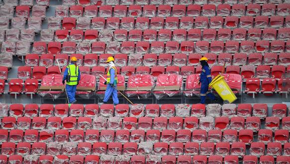 Das Bild zeigt Bauarbeiter auf der Tribüne eines Fußballstadions 