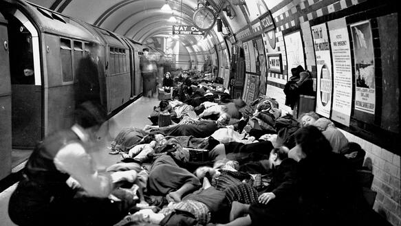 In einer Londoner U-Bahn-Station steht eine U-Bahn am Gleis, Menschen liegen auf dem Bahnsteig dicht an dicht.