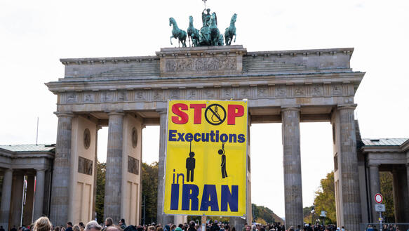Vor dem Brandenburger Tor in Berlin demonstrieren Menschen, sie halten ein Plakat hoch auf dem geschrieben steht "Stop Executions Iran".