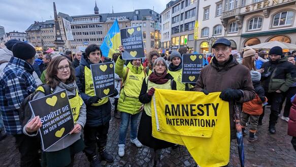 Das Bild zeigt mehrere Personen mit Schildern, die vor einem Gebäude stehen