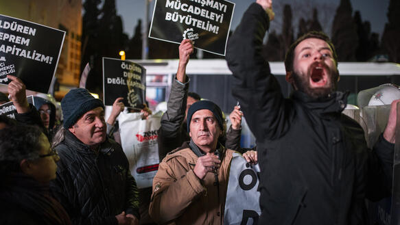 Das Foto zeigt eine Gruppe Menschen, die teilweise mit wütenden Gesichtern und geballten Fäusten Parolon rufen. Einige von ihnen halten Schilder hoch mit türkischer Schrift.