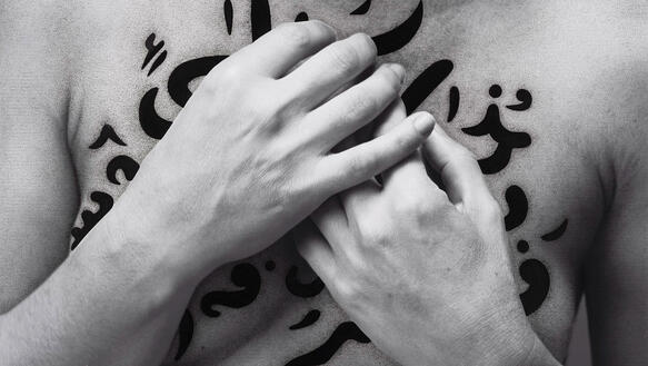 Arabische Schriftzeichen auf der Brust einer Frau, die ihre Hände davor verschränkt hält.