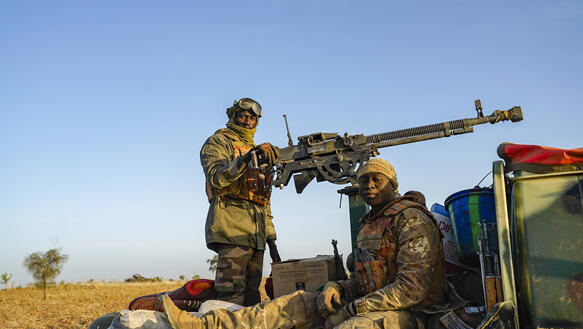 Das Foto zeigt zwei schwer bewaffnete Soldaten, die auf der Ladefläche eines Transporters sitzen und in die Kamera schauen.