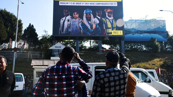 Zwei Männer blicken auf ein Plakate von Amnesty, das Arbeitsmigration nach Katar zum Thema hat.