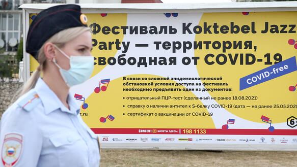 Das Foto zeigt im Seitenprofil eine Polizistin mit Mundschutz vor einem Plakat mit russischer Schrift.