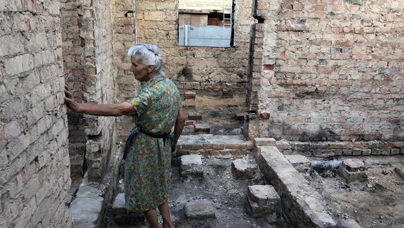 Das Bild zeigt eine ältere Frau in einer Hausruine