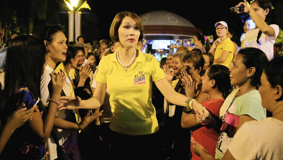 Das Foto zeigt eine Frau, die ein gelbes T-Shirt trägt und durch eine Menschenmenge läuft, die ihr zujubeln und teilweise Fotos von ihr machen.