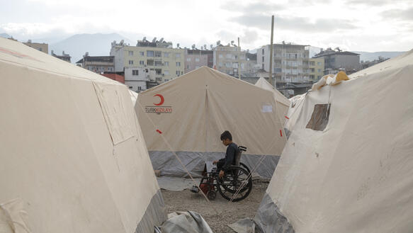 Das Bild zeigt einen  Jungen im Rollstuhl zwischen Zelten