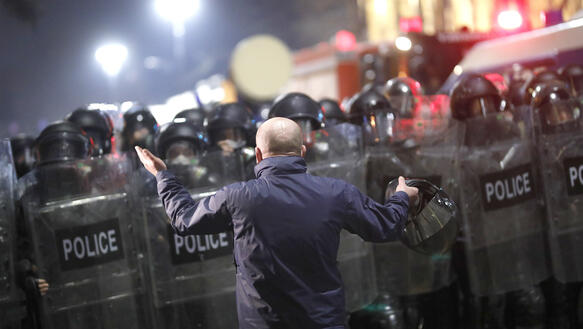 Ein Mann mit erhobenen Armen vor einer Polizeikette