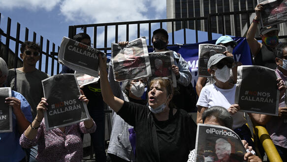 Protestierende halten eine Ausgabe von El Periodico in die Höhe, dahinter ein Gitter.