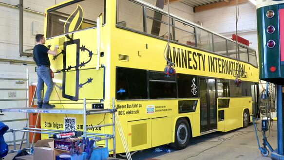 Das Bild zeigt einen gelben Bus, der in einer Werkstatt steht.