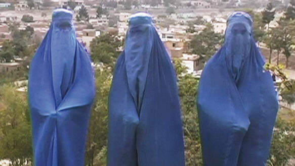 Drei afghanische Frauen in Burka stehen nebeneinander in der Natur, hinter ihnen ein Dorf in der Ferne.