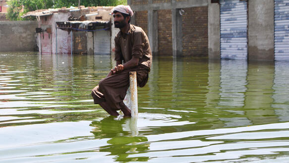 Ein Mann sitzt inmitten eines Hochwassers, dahinter Garagen