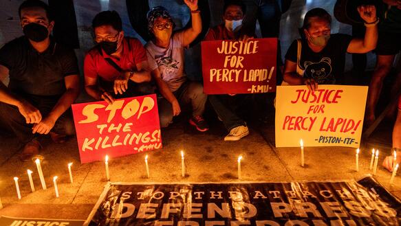 Menschen hinter Kerzen halten Plakate auf denen u.a. steht: „Justice for Percy Lapid“.
