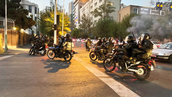 Iranische Polizisten auf Motorrädern in den Straßen Teherans, sie tragen Helme und Protektoren, manche von ihnen Schlagstöcke.