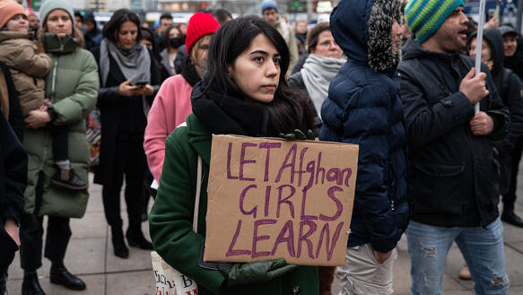Das Foto zeigt eine Frau bei einer Demonstration. Sie hält ein Pappschild vor sich mit der Aufschrift "Let afghan girls learn".