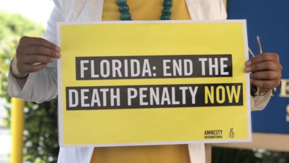 Eine Frau hält ein Plakat vor sich, auf dem steht "Florida: Ende the Deathy Penalty now!"