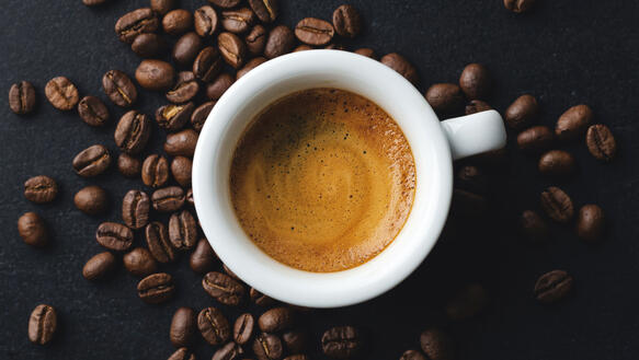 Eine Tasse mit frischem Espresso, daneben liegen Kaffeebohnen