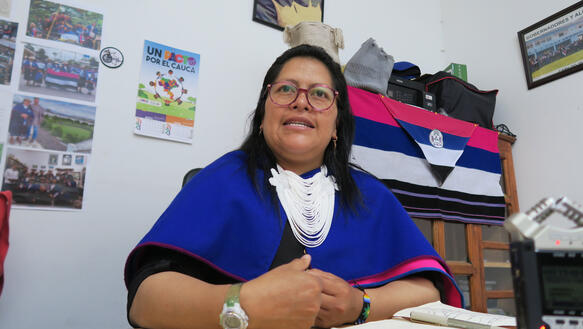 Eine indigene Frau trägt Halsschmuck und Brille, sie sitzt in einem Büro.