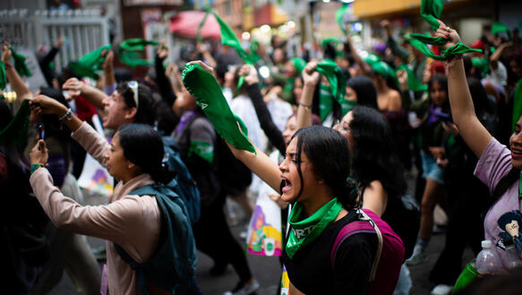 Das Foto zeigt eine große Menschenmenge, fast ausschließlich Frauen, die rufend und Tücher schwenkend durch die Straßen zieht.