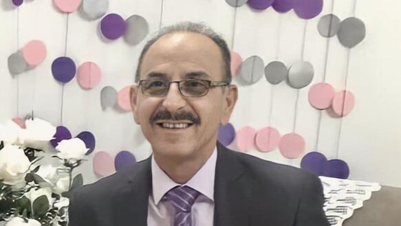 Porträtgoto von Bassem al-Zaak mit Brille und Schnäuzer. Er trägt einen Anzug und eine Krawatte und lächelt in die Kamera.
