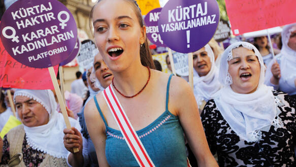 Türkische Frauen demonstrieren gegen ein Abtreibungsverbot, vorneweg läuft eine junge Frau mit Pferdeschwanz, hinter ihr ältere Frauen mit Kopftuch, die Schilder hochhalten, auf denen "Kurtaj Haktir Karar Kadinlarin Platformu" u.a. steht.