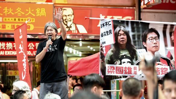 Das Foto zeigt Leung Kwok-hung, der bei einer Demonstration mit einem Mikrofon in der rechten Hand auf einer Bühene steht und zu der Menschenmenge spricht.