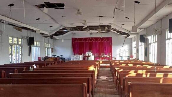 Das Foto zeigt eine Kirche von innen mit einer Reihe Sitzbänke. Die Decke ist beschädigt.