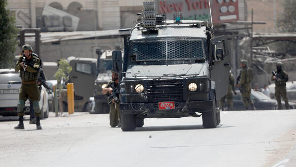 Das Bild zeigt eine Militärfahrzeug, daneben stehen Soldaten mit Waffen