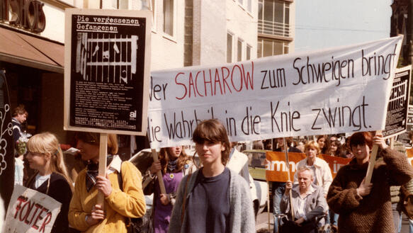 Menschen demonstrieren auf einer Straße, auf einem Banner steht "Wer Sacharow zum Schweigen bringt, die Wahrheit in die Knie zwingt"