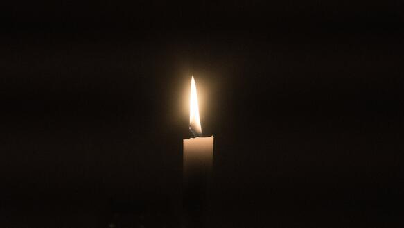 Das Bild zeigt eine Kerze auf schwarzem Hintergrund